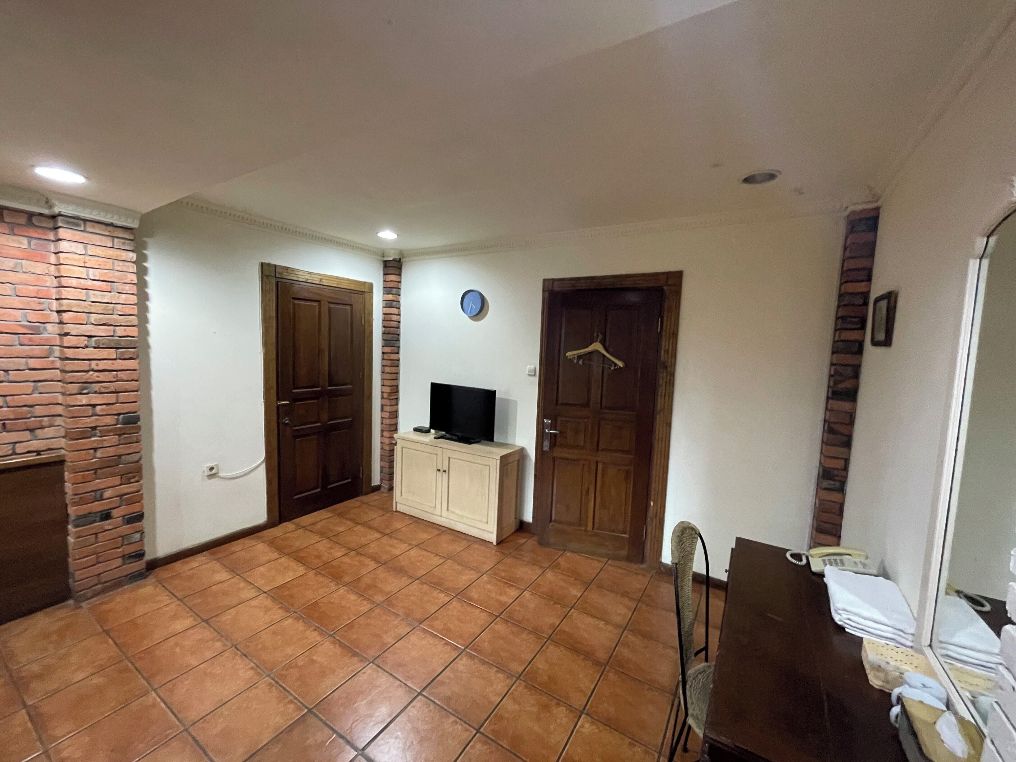Una habitación amplia con suelo de baldosas, un armario de madera, un televisor y una puerta con perchero.