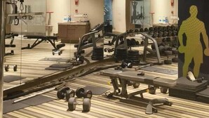 A gym with various exercise equipment, a mirrored wall, and a patterned carpet. - Homeiihood Stay Lucknow (Lucknow)