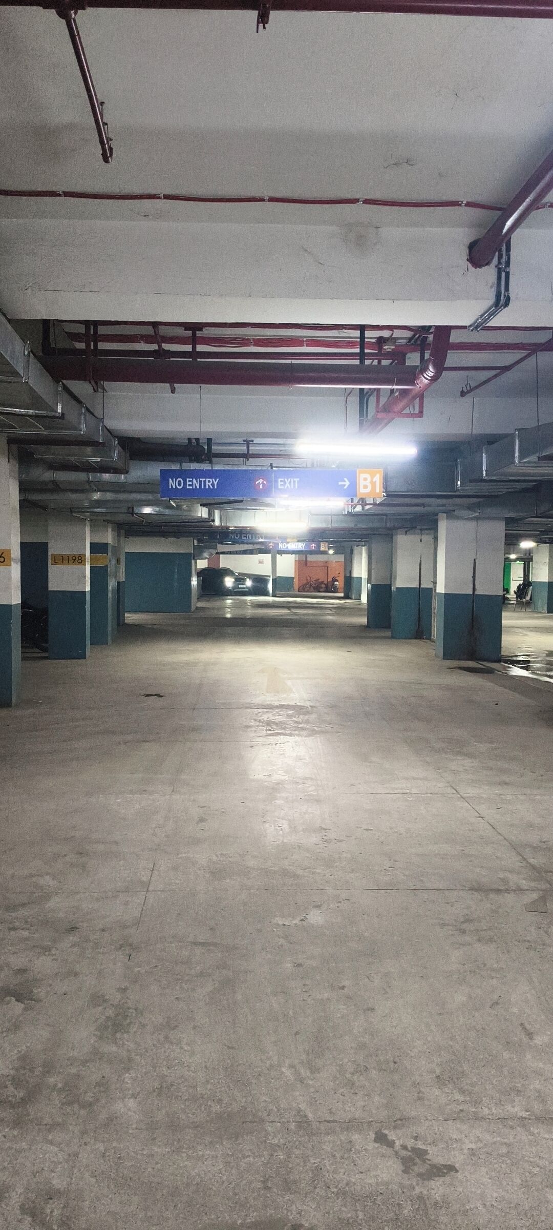 An underground parking garage with concrete floors and pillars, marked parking spaces, and directional signs indicating exits and no entry zones.