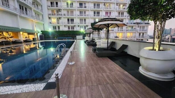 A rooftop pool area with lounge chairs and umbrellas, surrounded by a multi-story building with balconies. - Homeiihood Stay Lucknow (Lucknow)