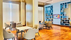 A modern interior with a wooden floor, white and beige chairs, a long table, and a blue bookshelf with books. - Homeiihood Stay Lucknow (Lucknow)