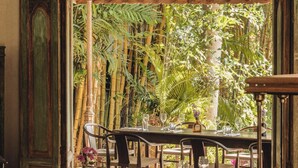 Un espace repas avec des tables et des chaises, un luminaire suspendu et une vue sur un jardin luxuriant.