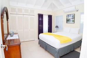 A bedroom with a bed, a dresser, a mirror, a window with curtains, and a wall-mounted air conditioner. - Cozy 3BR Villa w/ Poolside Gym, AC & WiFi near Ocho Rios (Ocho Rios)