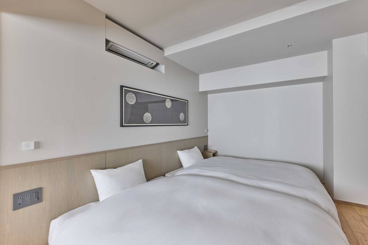 Ein modernes Hotelzimmer mit einem großen Bett, einer Wand-Klimaanlage, einem gerahmten Bild und einem Nachttisch.
