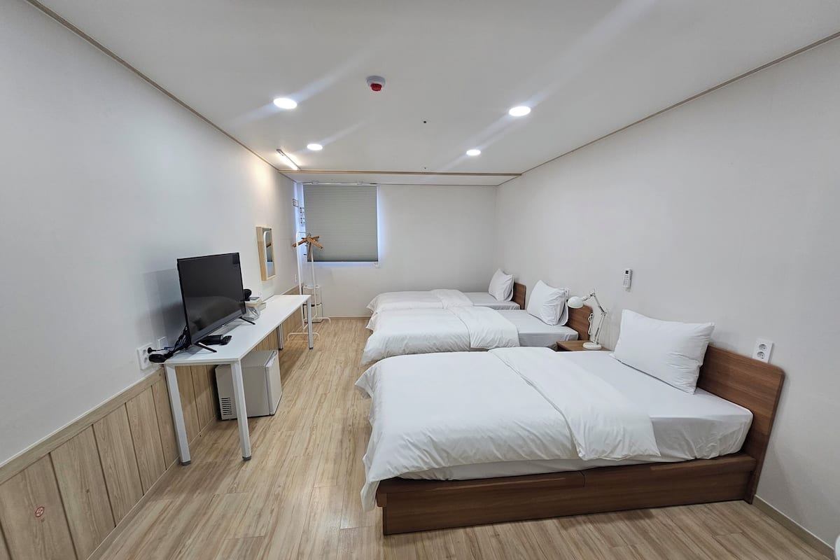 A hotel room with two single beds, a desk with a computer, a TV, and a window with blinds.