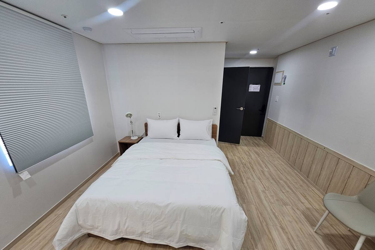 A hotel room with a large bed, a bedside table with a lamp, a wooden floor, and a door leading to another room.