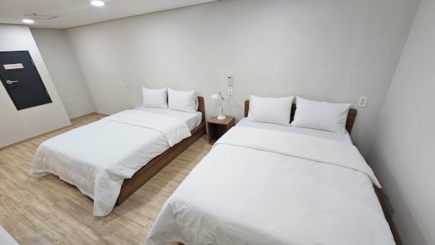 A hotel room with two single beds, wooden headboards, white bedding, a bedside table with a lamp, and a door with a sign. - BonghwangINN BonghwangMansion2 (Gyeongju)