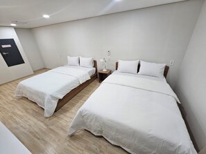 Habitación de hotel con dos camas individuales, cabeceros de madera, ropa de cama blanca, una mesita de noche con lámpara y una puerta con un cartel.