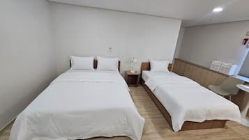 A hotel room with two single beds, a small table, a chair, and a bedside table with a lamp.