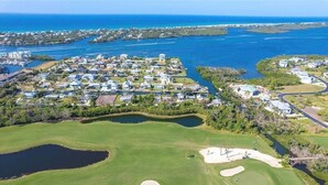 Vista aerea di un campo da golf costiero con zone residenziali nelle vicinanze, immerso nell'acqua e nel verde.