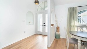 Un interno luminoso e moderno con pavimento in legno, zona pranzo con tavolo e sedie, una porta in vetro che dà su un'altra stanza e un lampadario.