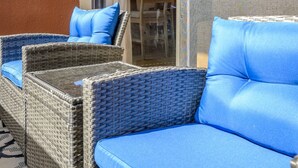 Un sofá de mimbre con cojines azules y una puerta de cristal que da a un espacio interior.