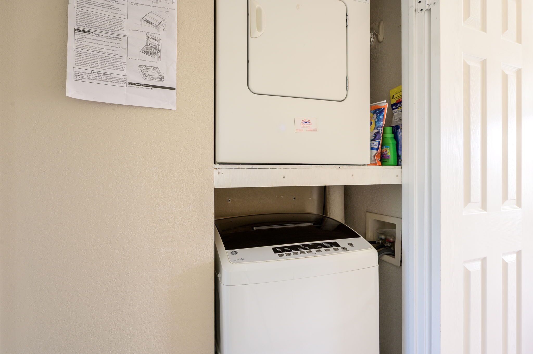 A laundry room with a washing machine and dryer, a door, and a shelf with cleaning supplies.
