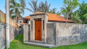 A small, private entrance with a wooden door, surrounded by a concrete wall and a grassy area. - Villa Deruja Ubud (Ubud)