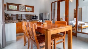 A modern kitchen with a wooden dining table and chairs, a microwave, and a refrigerator. - Villa Deruja Ubud (Ubud)