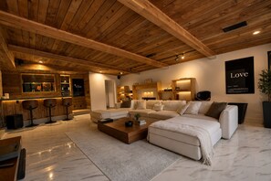 Sala de estar moderna com teto de madeira, sofá seccional, mesa de centro e área de bar com banquetas.