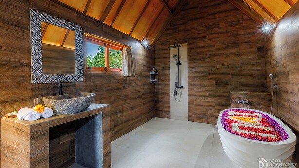 A bathroom with a wooden ceiling, a large sink, a shower, and a bathtub with a flower arrangement.