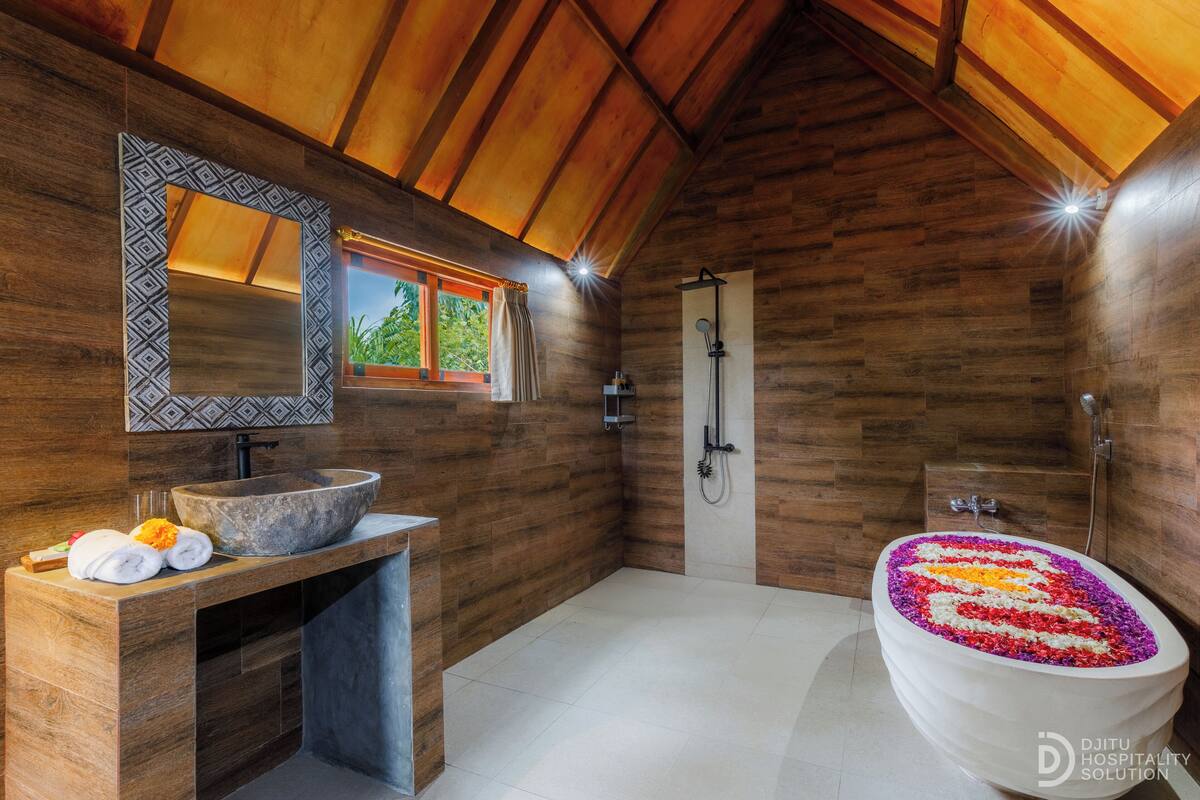 Une salle de bain avec un plafond en bois, un grand lavabo, une douche et une baignoire agrémentée d’un arrangement floral.