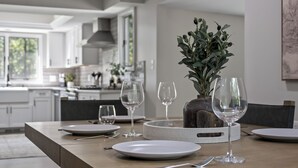 A dining table set with plates, cutlery, and wine glasses, with a vase of greenery in the center.