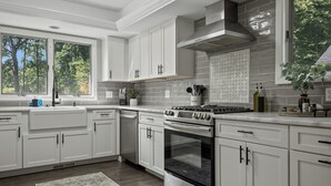 A modern kitchen with white cabinetry, a stainless steel stove, and a large window.