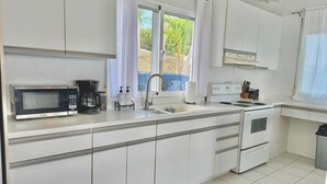 A modern kitchen with white cabinets, a built-in microwave, a coffee maker, and a stove.