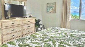 Une chambre à coucher avec un lit, une commode, un téléviseur, un tableau et une fenêtre donnant sur un beau paysage.