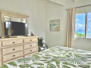 Une chambre à coucher avec un lit, une commode, un téléviseur, un tableau et une fenêtre donnant sur un beau paysage.