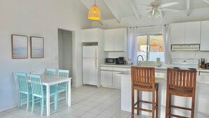 Une cuisine moderne avec des meubles blancs, un réfrigérateur blanc, un four à micro-ondes et une cuisinière. On y trouve également un coin repas avec une table blanche et des chaises turquoise.