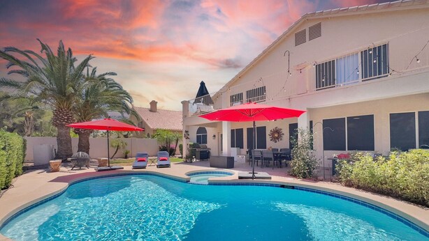 Une piscine avec des chaises longues et des parasols, un espace patio et un bâtiment doté d’un balcon.