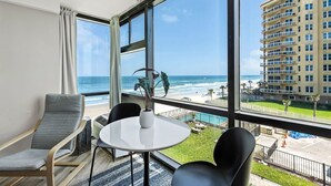 Ein Hotelzimmer mit großem Fenster mit Blick auf einen Strand und ein Hochhaus.