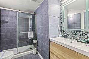 A modern bathroom with a glass-enclosed shower, a white toilet, and a sink with a mirror above it. - NEW! Escape `Two` Oceanside - Updated Double Studio w/ Pool & Beach Access (Daytona Beach)