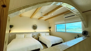 A bedroom with two beds, a ceiling fan, a large window with a view, and a small table. - Resort Villa KAPUKA SESOKOJIMA (Motobu)