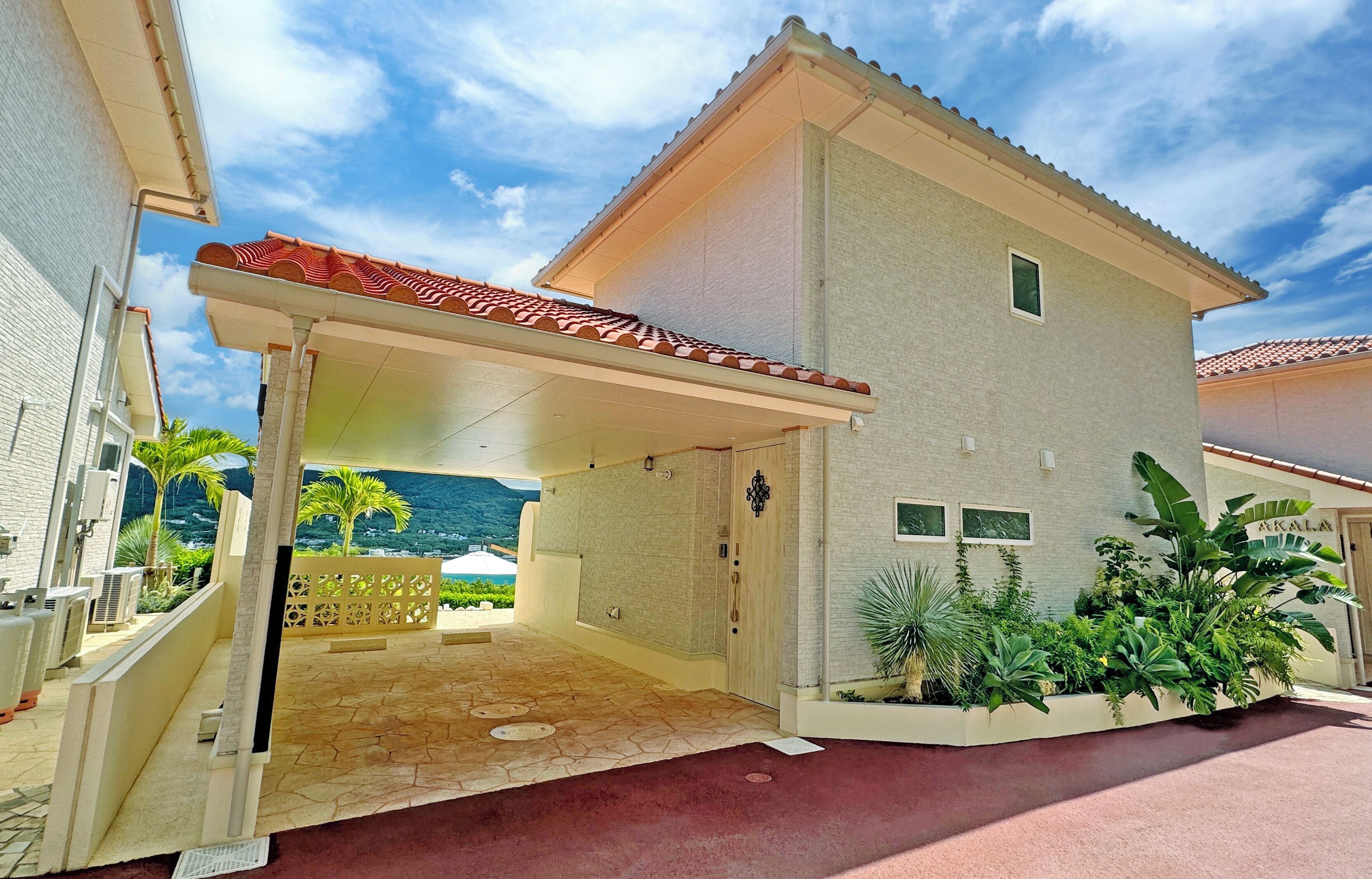 A two-story house with a covered patio, a stone-tiled entrance, and a landscaped garden with tropical plants.