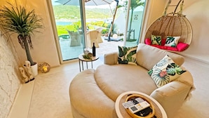 A cozy living area with a sofa, a hanging chair, and a small table with a bottle and remote control. - Resort Villa KAPUKA SESOKOJIMA (Motobu)