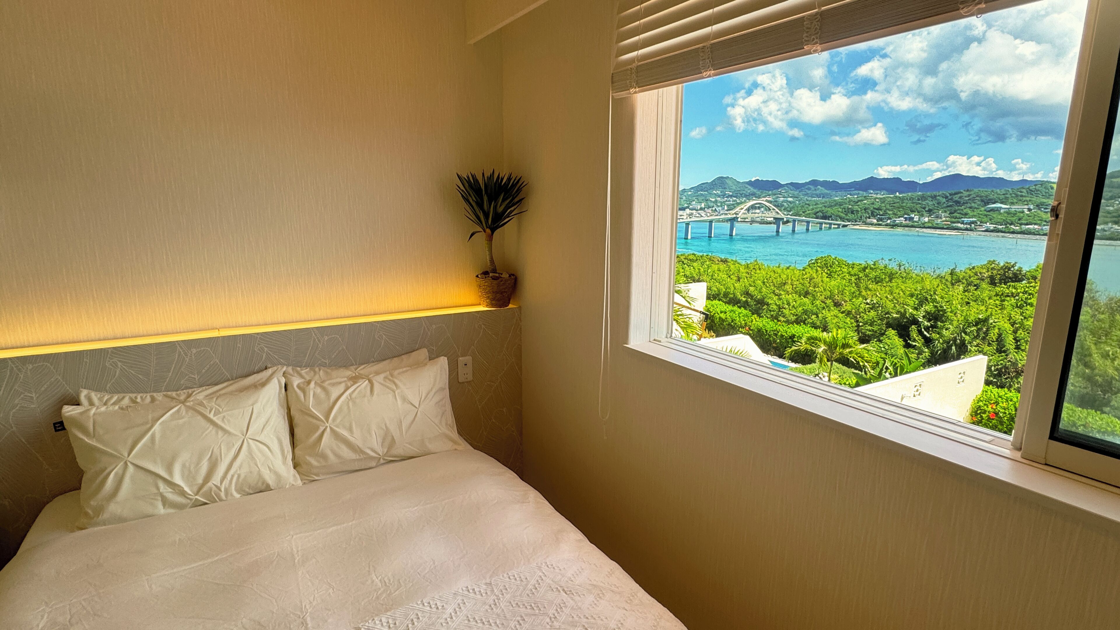 A bedroom with a bed, a window with a view of a bridge and greenery.