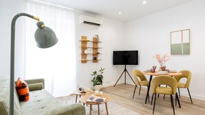 A modern living room with a sofa, a coffee table, a TV, a dining area with chairs, and a potted plant. - Apartment + Work Area in Retiro (Madrid)