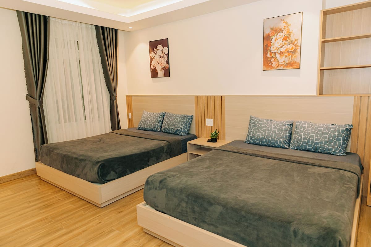 A hotel room with two beds, a nightstand, a small plant, and artwork on the walls.