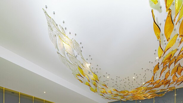 A modern interior with a large glass partition, a white flower arrangement, and a ceiling with a golden design. - An Mai Boutique (Lam Vien - Da Lat)