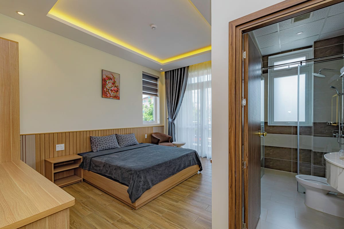 A modern bedroom with a wooden bed, a nightstand, and a bathroom with a shower and toilet.