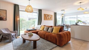 Ein modernes Wohnzimmer mit einer Eckcouch, einem Couchtisch und einem Essbereich mit Küche im Hintergrund.