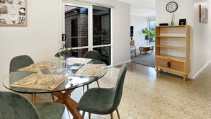 Un saló modern amb una taula de dinar de vidre, cadires verdes, una prestatgeria i una llar de foc.