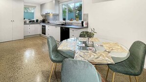 Una cuina moderna amb armaris blancs, una illa central i una zona de menjador amb taula i cadires de vidre.
