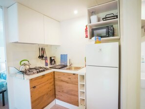 Cozinha compacta com armários brancos, micro-ondas, fogão a gás e geladeira.