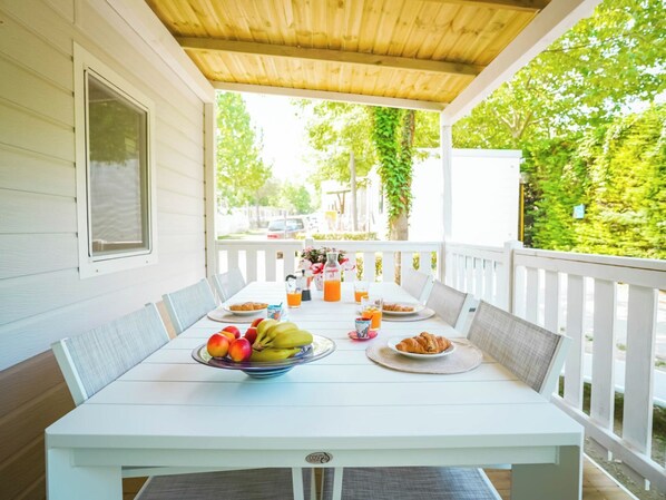 A covered porch with a table set for breakfast, including fruits, pastries, and drinks.