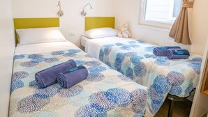 A hotel room with two beds, each with a patterned bedspread, a small shelf above the beds, and a window with curtains.