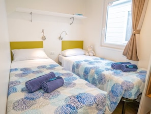 A hotel room with two beds, each with a patterned bedspread, a small shelf above the beds, and a window with curtains.