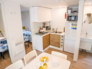 Cocina compacta con estufa, lavaplatos y microondas. Cuenta con una mesa de comedor, sillas y un refrigerador pequeño.