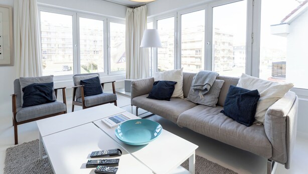 Een moderne woonkamer met een bank, twee fauteuils, een salontafel en een groot raam met uitzicht op de stad.