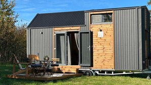 Une petite cabane moderne avec une porte coulissante, une petite terrasse avec des sièges d’extérieur et une fenêtre.