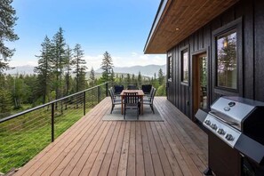 Una terraza con una parrilla y una mesa con sillas, con vista a un área boscosa y montañas al fondo.